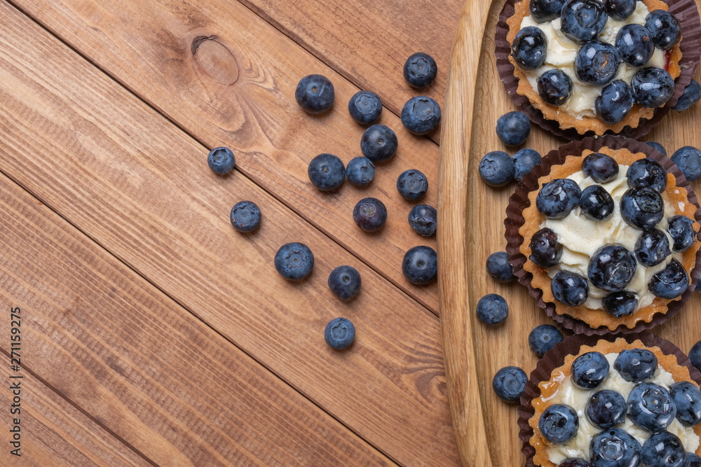 three bilberry tartlet on a wooden plate on the table, bilberry baked shells, fruit cupcake with blueberry three bilberry tartlet on a wooden plate on the table, bilberry baked shells, fruit cupcake with blueberry
