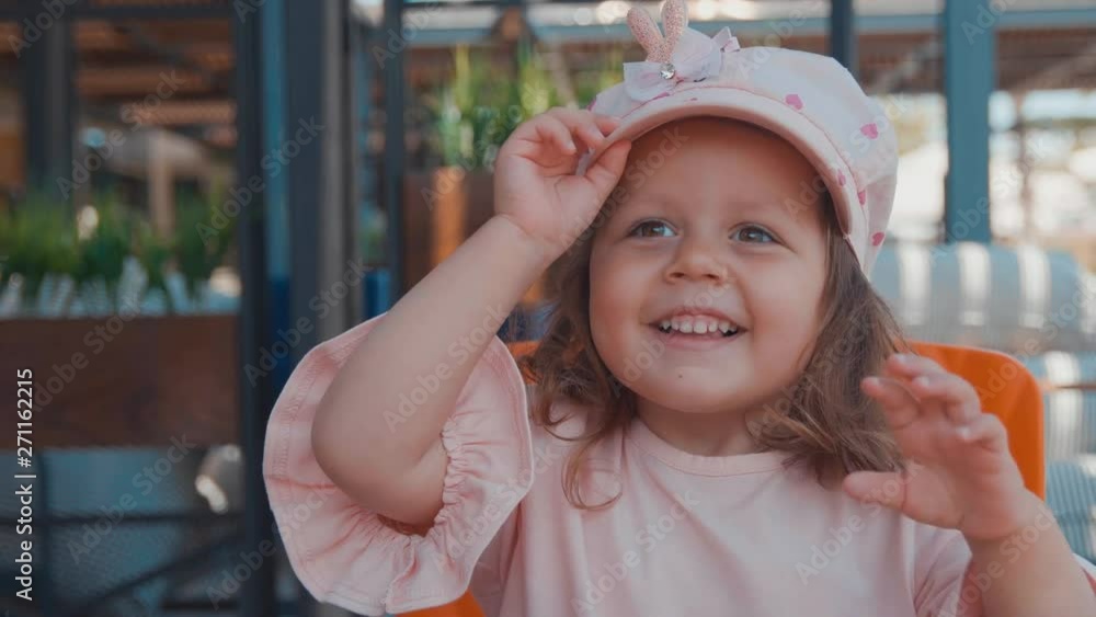 Portrait of little beautiful girl in pink cap smiling to the camera and flaps hand. Slow motion Portrait of little beautiful girl in pink cap smiling to the camera and flaps hand. Slow motion