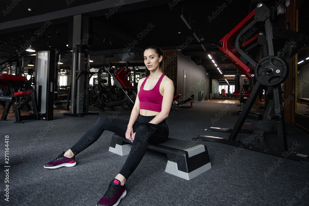 Close up portrait of young pretty european fitness woman sitting on the step platform at the gym. Breaking relax while exercise workout. Concept of health and sport lifestyle. Athletic Body. Close up portrait of young pretty european fitness woman sitting on the step platform at the gym. Breaking relax while exercise workout. Concept of health and sport lifestyle. Athletic Body.
