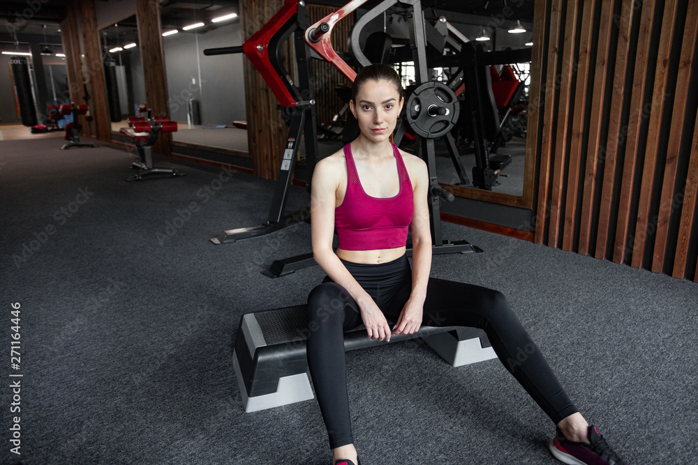 Close up portrait of young pretty european fitness woman sitting on the step platform at the gym. Breaking relax while exercise workout. Concept of health and sport lifestyle. Athletic Body.