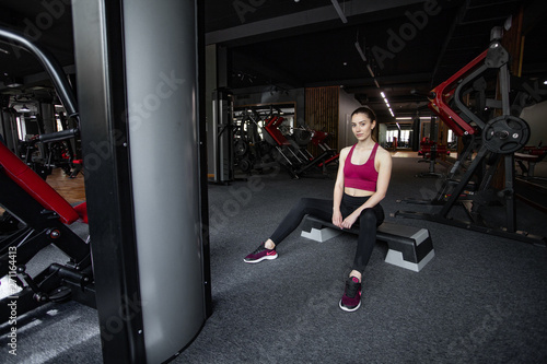 Close up portrait of young pretty european fitness woman sitting on the step platform at the gym. Breaking relax while exercise workout. Concept of health and sport lifestyle. Athletic Body.