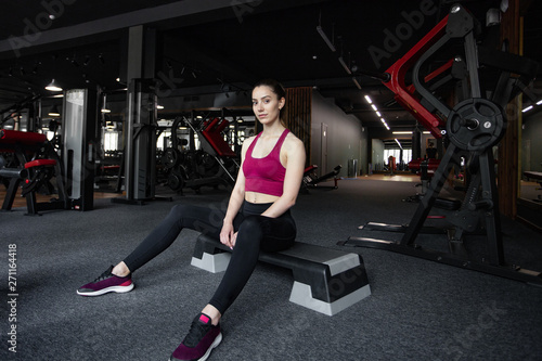 Close up portrait of young pretty european fitness woman sitting on the step platform at the gym. Breaking relax while exercise workout. Concept of health and sport lifestyle. Athletic Body.