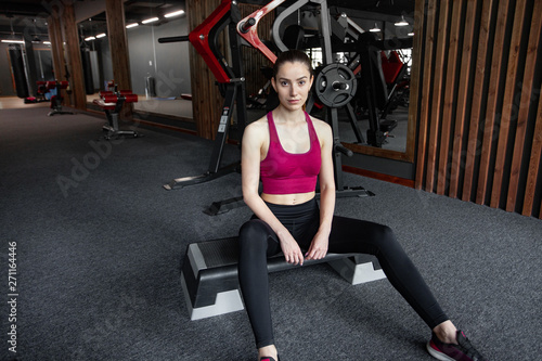 Close up portrait of young pretty european fitness woman sitting on the step platform at the gym. Breaking relax while exercise workout. Concept of health and sport lifestyle. Athletic Body.