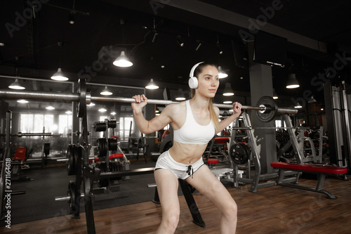 Young pretty muscular woman doing fitness exercise. Squat workout in gym. Stylish black interior of modern fitness gym. Concept of health and sport lifestyle. Athletic Body. .