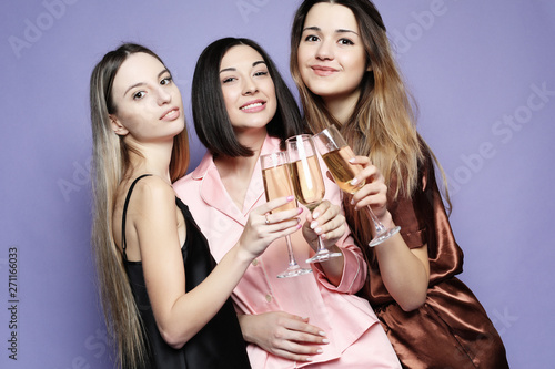 three beautiful girls dressed in pajamas drink champagne and have fun