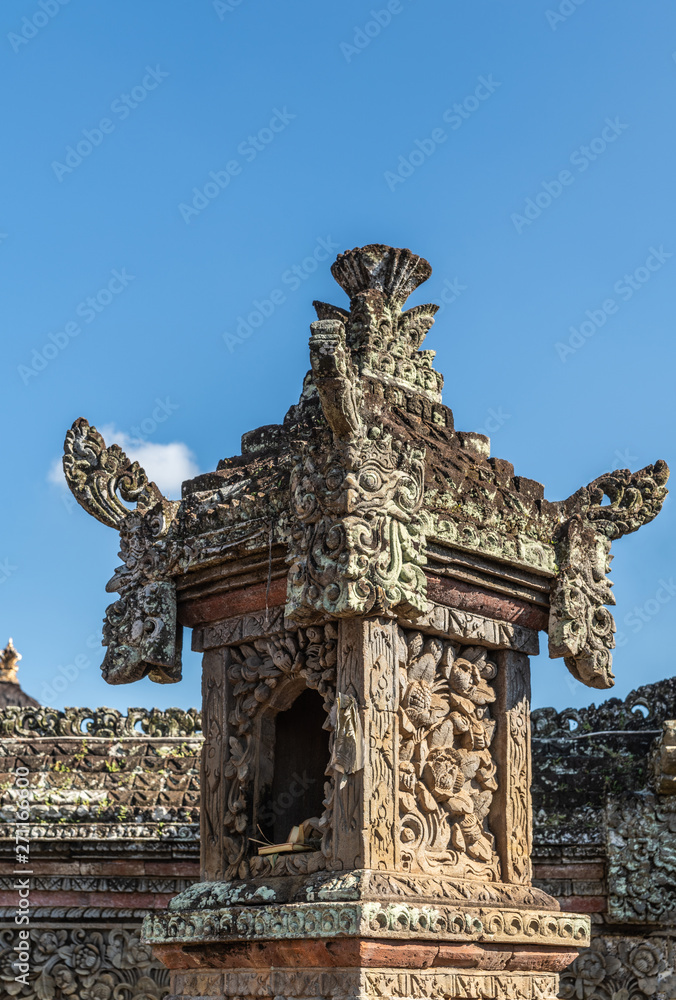 Ubud, Bali, Indonesia - February 26, 2019: Batuan Temple. Closeup of gray stone shrine on top of pillar under blue sky. Green and black mold.
