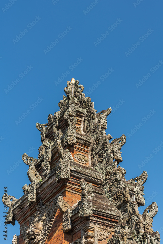 Ubud, Bali, Indonesia - February 26, 2019: Batuan Temple. Closeup of gray stone spire of Kori Agung, main shrine under blue sky. Red bricks and gray stone ornaments covered by mold.