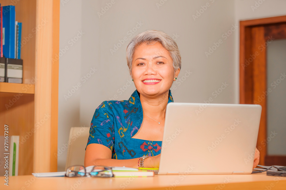 Lifestyle portrait of Happy and attractive elegant middle aged Asian business woman working smiling at office computer desk feeling positive and successful Lifestyle portrait of Happy and attractive elegant middle aged Asian business woman working smiling at office computer desk feeling positive and successful