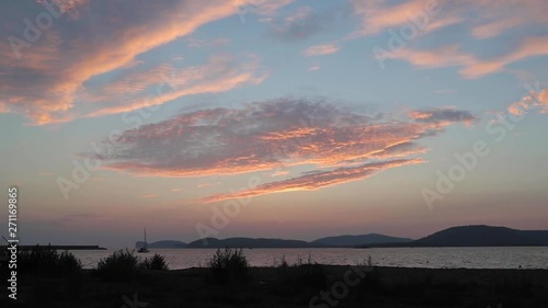 Silhouette Alghero coastline foreground under hazy layered mountain ranges below colourful orange sunset skyline.