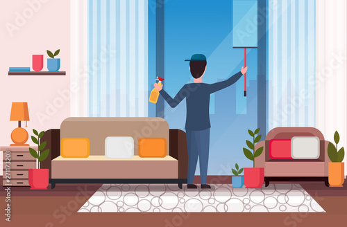 male janitor using shower wiper squeegee and spray plastic bottle man cleaner wiping glass window cleaning service concept modern living room interior full length flat horizontal