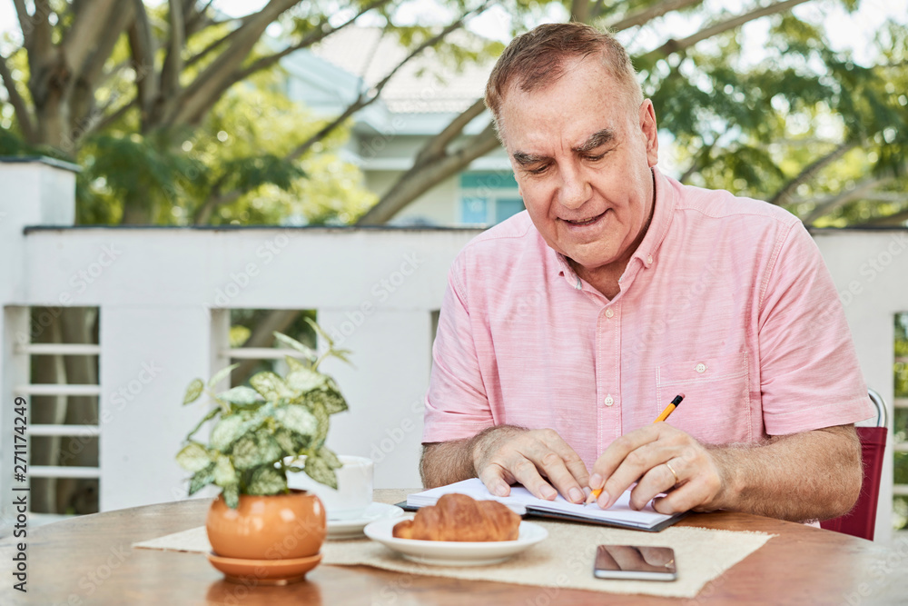 Positive aged man sitting at table in outdoor cafe and writing in planner Positive aged man sitting at table in outdoor cafe and writing in planner