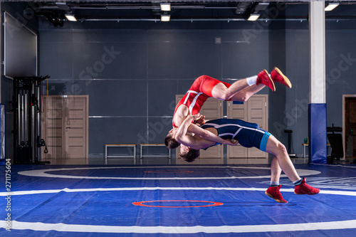 The concept of fair wrestling. Two greco-roman wrestlers in red and blue uniform wrestling on a wrestling carpet in the gym.The concept of fair wrestling