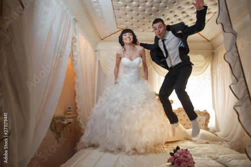 bride and groom having fun jumping on the bed joyful pillow fighting happiness