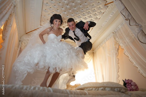 bride and groom having fun jumping on the bed joyful pillow fighting happiness