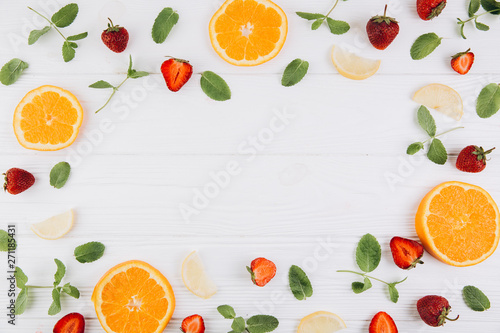 Summer colorful flat lay. Pattern made of citrus fruits  leaves and strawberries on the white wooden table. Top view and copy space