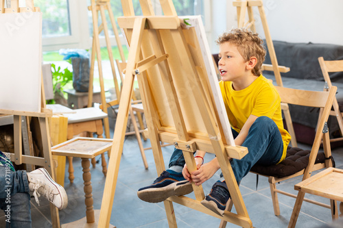 Schoolboy sitting near painting easel in art school