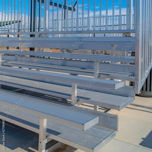 Square frame Raised tiered rows of benches with railings at a sports filed on a sunny day
