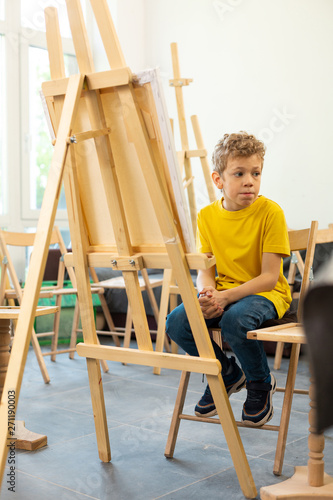 Cute funny boy wearing yellow t-shirt sitting in art school