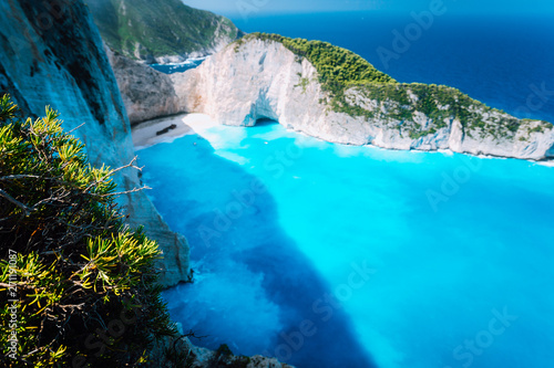 Wide view of Navagio beach with green vegetation in foreground. Famous landscape of Zakinthos island, Greece