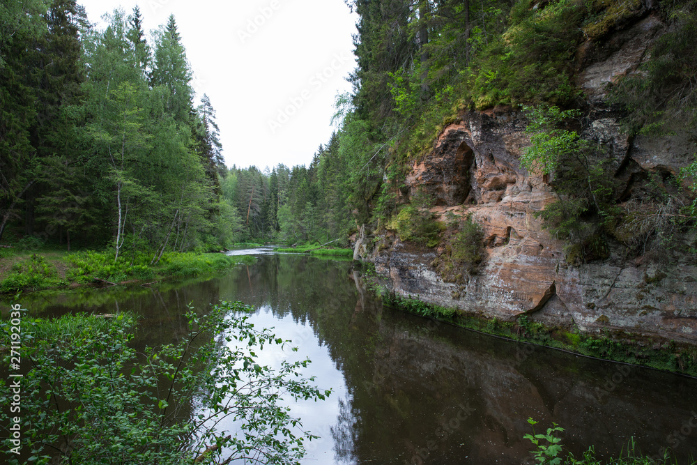 City Straupe, Latvian Republic. Red rocks and river Brasla. Green and overgrown forest. Jun 1. 2019 Travel photo. City Straupe, Latvian Republic. Red rocks and river Brasla. Green and overgrown forest. Jun 1. 2019 Travel photo.