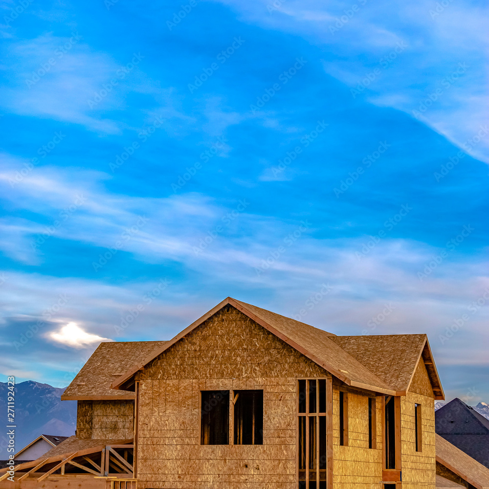 Square frame Exterior of a house under construction against vivid blue sky with clouds Square frame Exterior of a house under construction against vivid blue sky with clouds