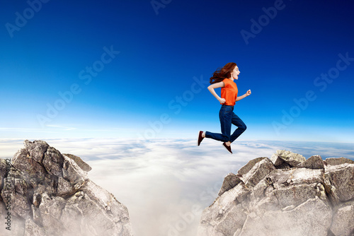 Redhead woman jumps through the gap between hills.