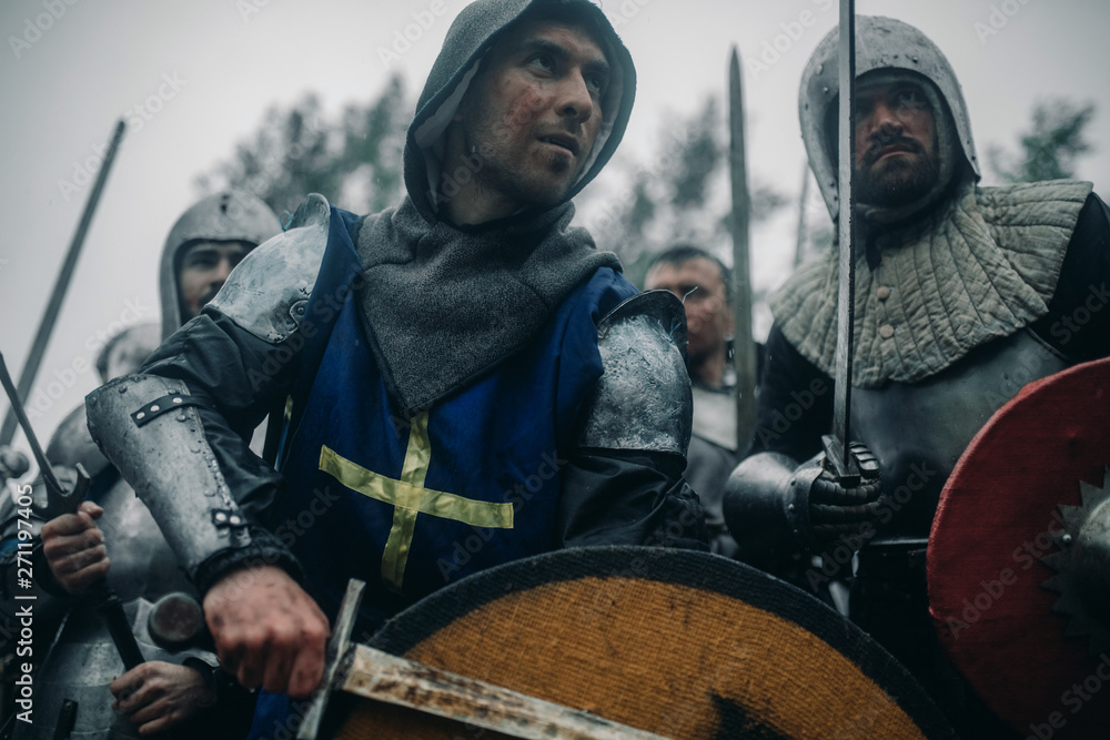 Squad of medieval knights of the Crusaders in armors with their swords preparing to attack.