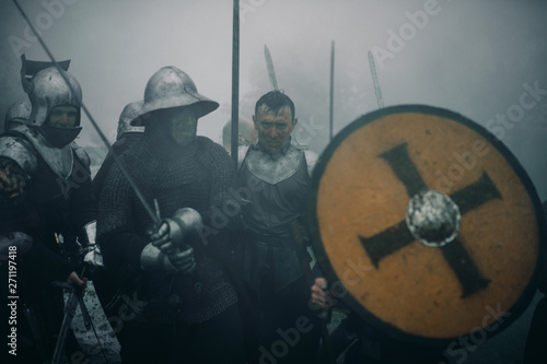 Combat squad of medieval knights of the Crusaders stand in armors preparing to attack in misty morning. photo