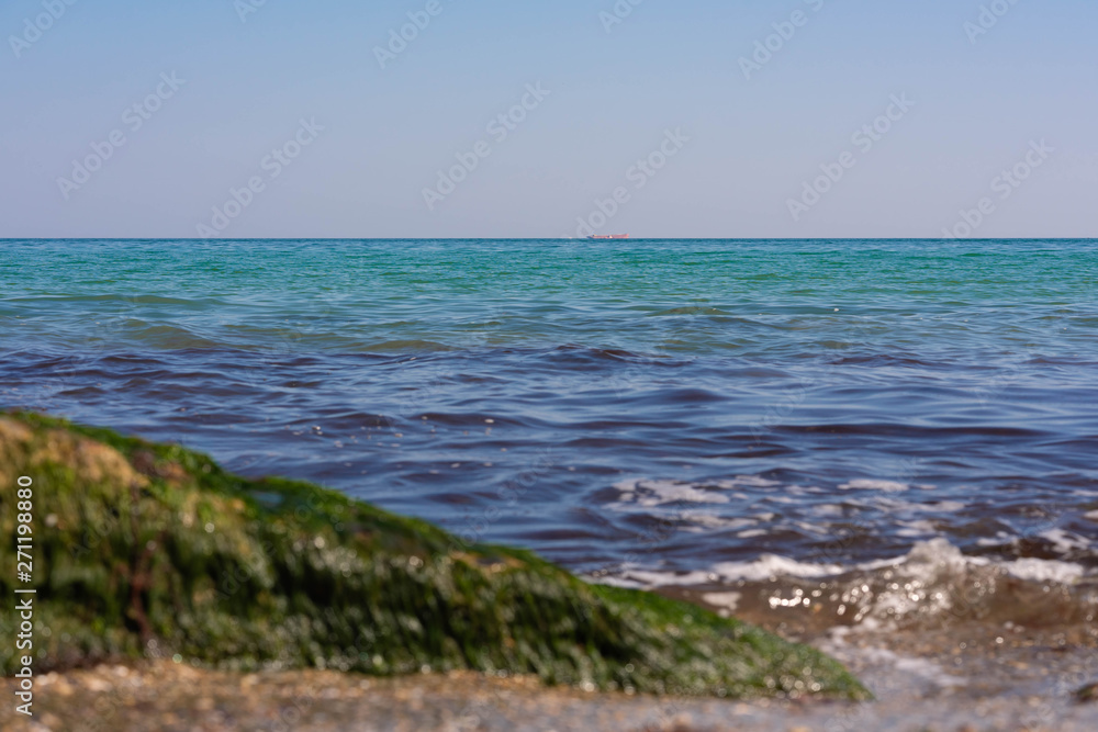 View of the Black Sea on a clear sunny day. On the shore, stones and sand, ships on the horizon. Blue sky and beautiful clouds.