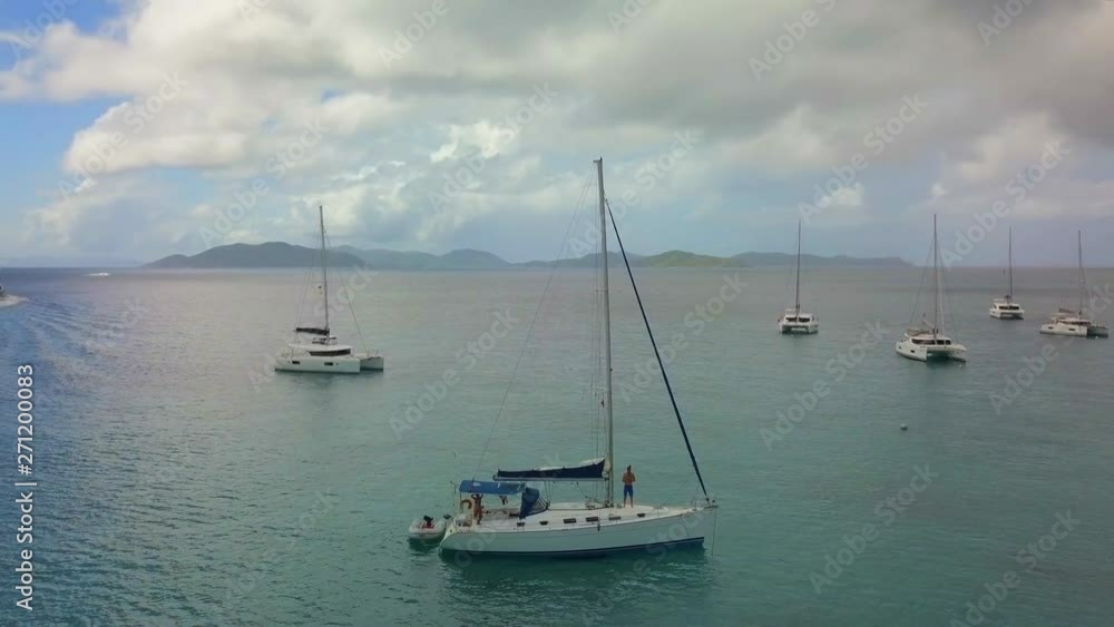 Aerial: Group of Boats Anchored in Tropical Ocean and Another Boat Drives Off in St. Croix, US Virgin Islands