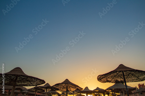 Tops of sun parasols standing at summer beach isolated on morning sunrise blue and orange background. Happy and safe sunbathing concept. Horizontal color photography.