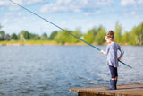 Cute little child girl in rubber boots fishing from wooden pier on a lake. Family leisure activity during summer sunny day