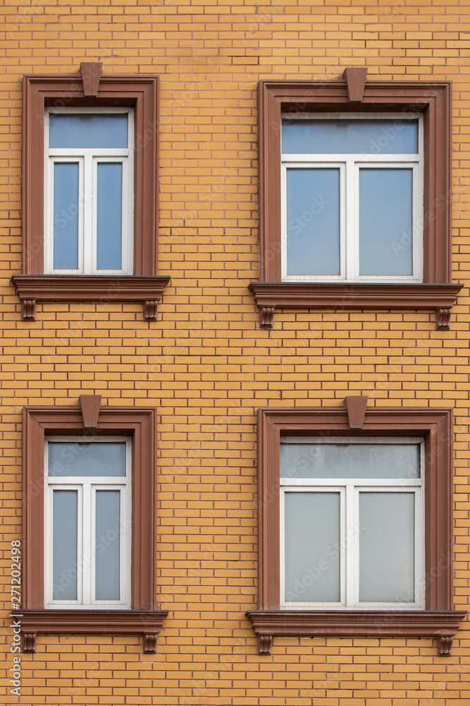 4 plastic windows in the brick house of yellow bricks. Beautiful windows with moldings and brown trim. Modern design of windows, construction of residential buildings