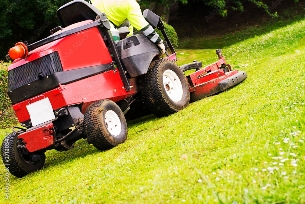 Obraz premium gardener with lawn mower vehicle cutting green grass on city garden