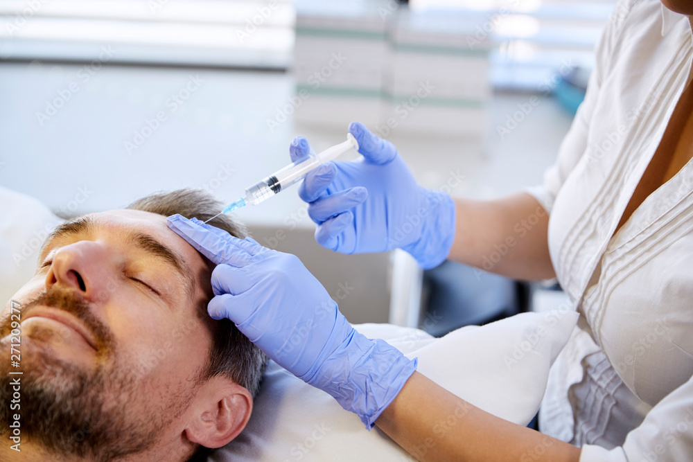 Fototapeta premium Female Beautician Giving Mature Male Patient Botox Injection In Forehead