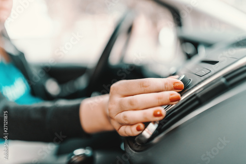 Close up of young pregnant Caucasian woman driving car and changing radio station.
