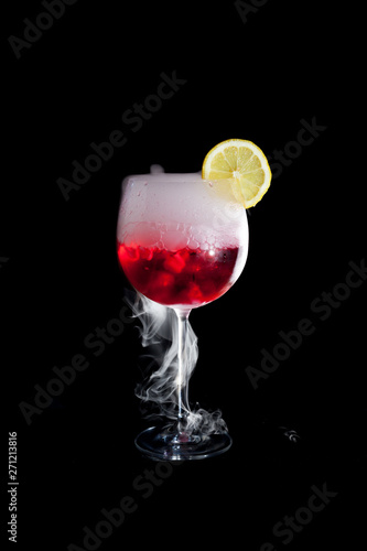 A cup of red cold cocktail with dry ice smoke and a lemon slice