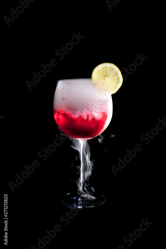 A cup of red cold cocktail with dry ice smoke and a lemon slice