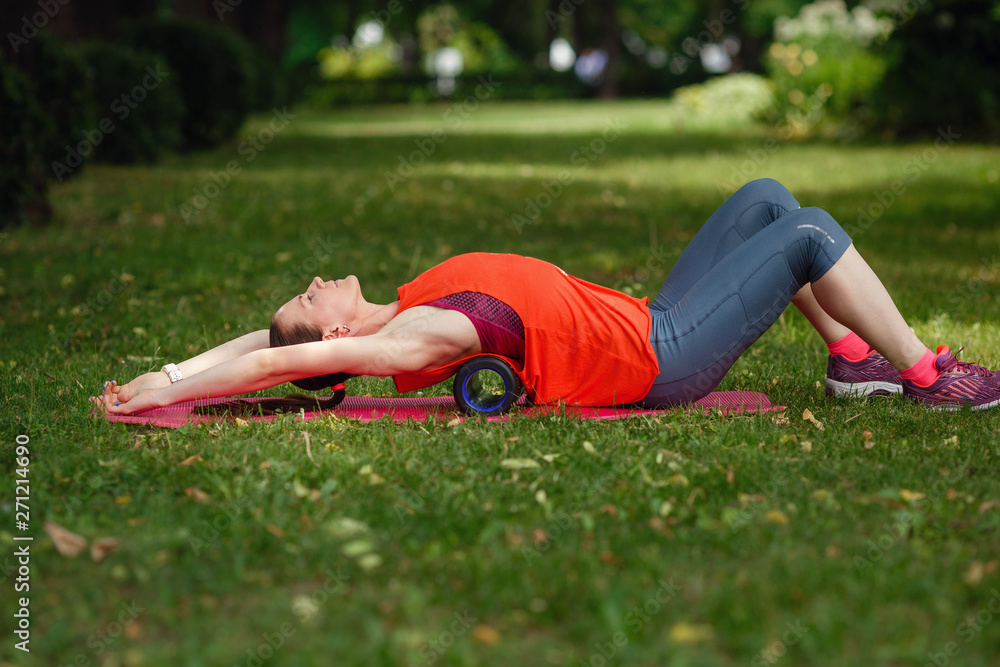 Fototapeta premium A young woman does stretching with a special roller in the park.
