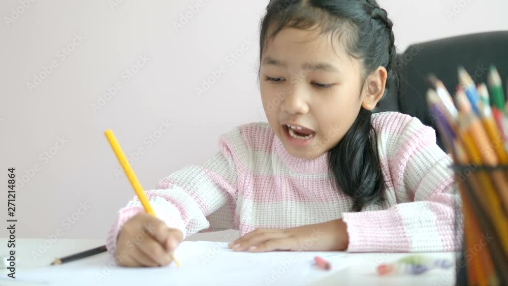 Little Asian girl using the pencil to write on the paper doing homework and smile with happiness for education concept select focus shallow depth of field Little Asian girl using the pencil to write on the paper doing homework and smile with happiness for education concept select focus shallow depth of field