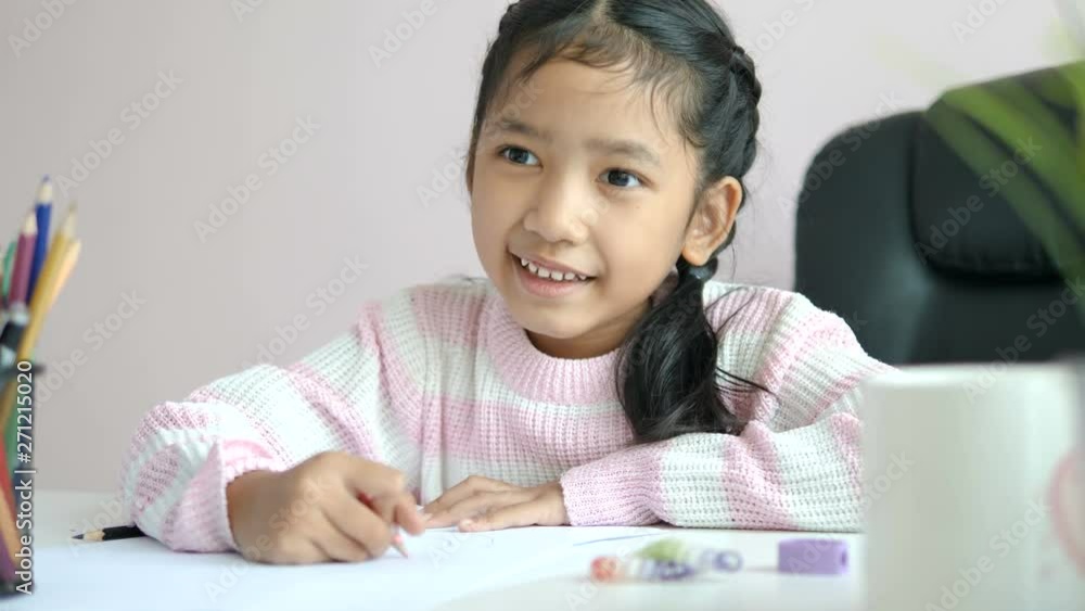 Little Asian girl using the pencil to write on the paper doing homework and smile with happiness for education concept select focus shallow depth of field Little Asian girl using the pencil to write on the paper doing homework and smile with happiness for education concept select focus shallow depth of field