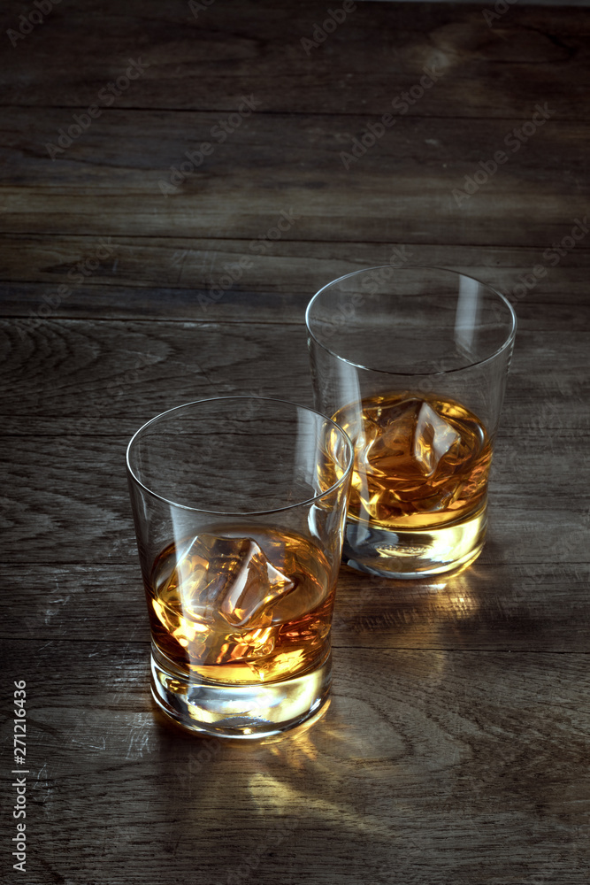 close up view of two glasses with ice and whiskey on wooden background
