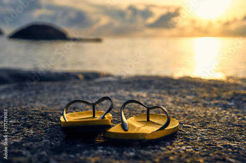  Slippers on a rock by the sea on a background of dawn and sun                             