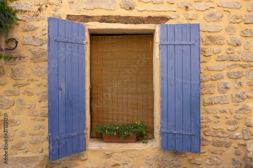 Vintage window with blue shutters on a yellow wall in the Provence France