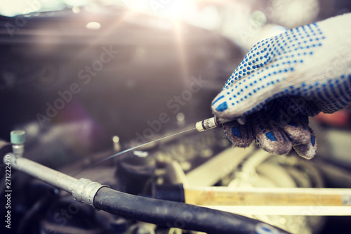 car service, repair, maintenance and people concept - auto mechanic man with dipstick and lamp checking for motor oil level at workshop