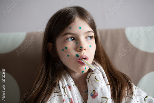 Fotografie a girl with chickenpox measures her temperature
