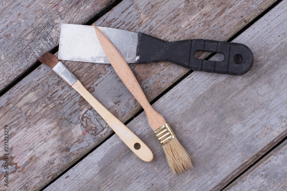 Construction tools on wooden boards background. Metal spatula with plastic handle and two paint brushes on rustic planks. Construction tools on wooden boards background. Metal spatula with plastic handle and two paint brushes on rustic planks.