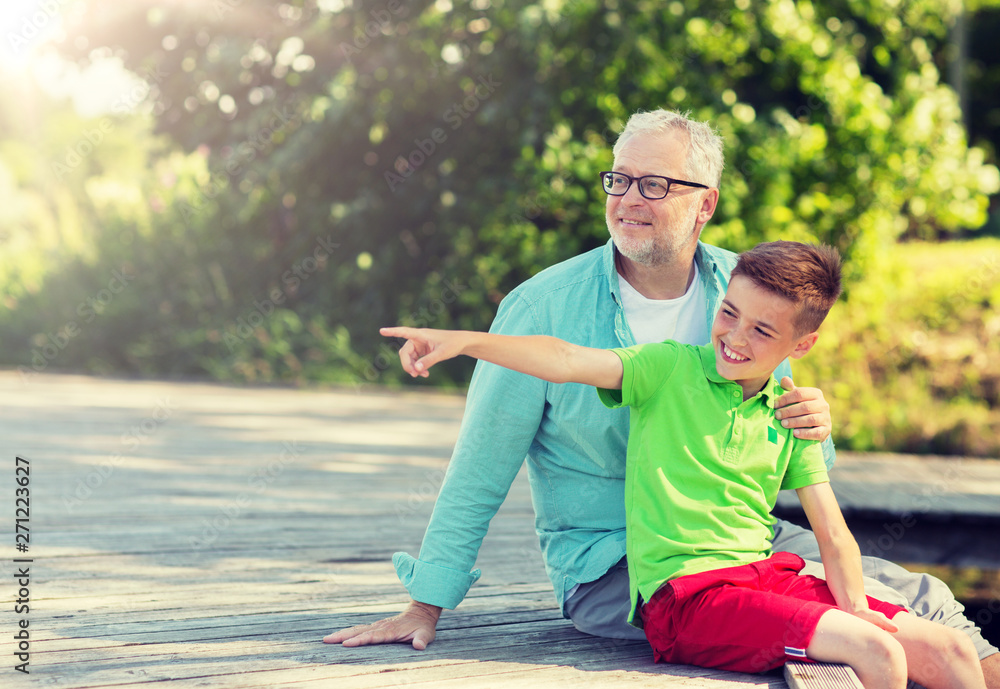 Obraz premium family, generation, communication and people concept - happy grandfather and grandson sitting on river berth