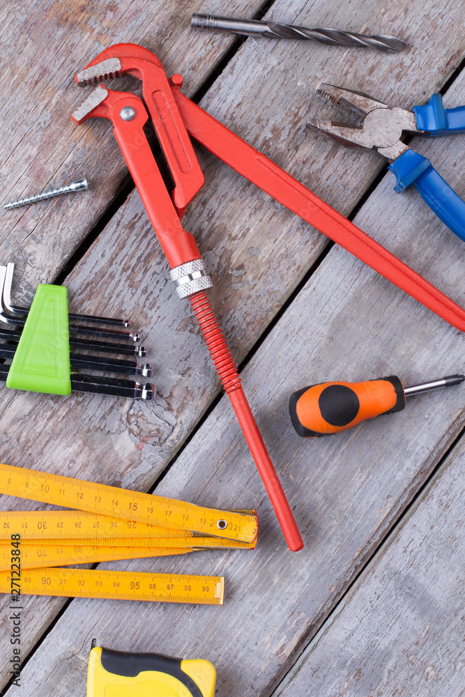 Tools for repair and construction. Screwdriver, pipe wrench pliers, measuring tape, folding ruler, drill bit and screw on wooden background. Tools for repair and construction. Screwdriver, pipe wrench pliers, measuring tape, folding ruler, drill bit and screw on wooden background.