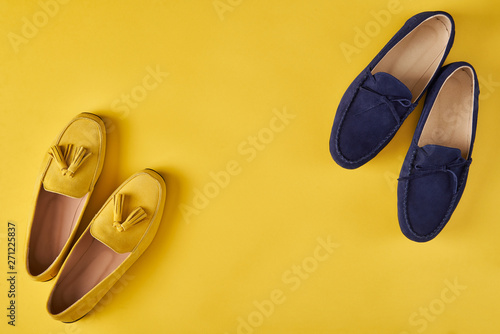 Dark blue suede man's and yellow woman's moccasins shoes over yellow background, photo